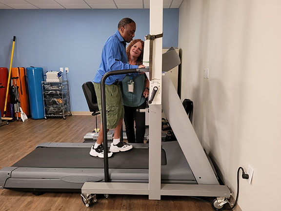 smiling man walking on treadmill, therapist standing smiling