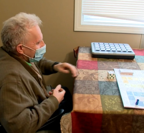 man in wheelchair playing a board game|Game board with game piece and dice|News 12 logo
