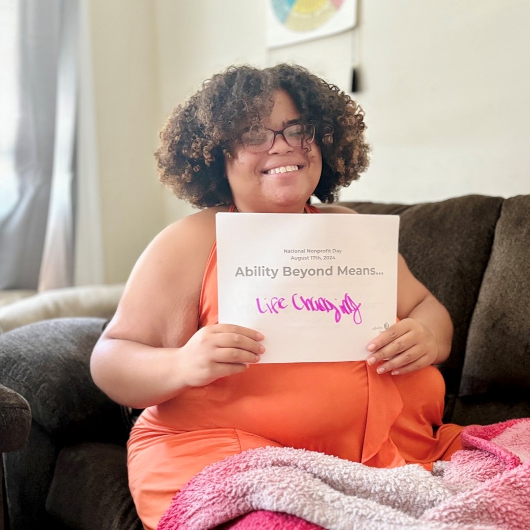 Nina holds a sign that says Ability Beyond Means, Life Changing.